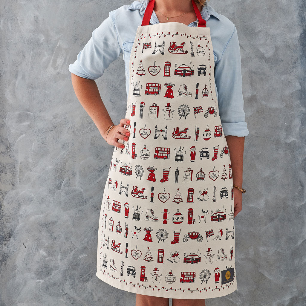 Adult's Christmas apron featuring various London Christmas icons, Red strapped London icons Christmas apron, Hand illustrated Christmas apron, Cotton Christmas apron featuring iconic London Christmas favorites, Christmas apron with repeating London Christ