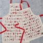 Children's London Christmas apron featuring repeating London landmarks, Kids kitchen apron featuring iconic London Christmas icons, Children's Christmas kitchen apron with red strap, Cotton Children's Christmas apron featuring ice skates and The London Ey